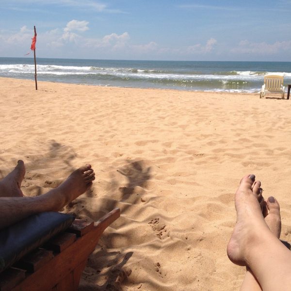 Blick über entspannt auf einer Liege ausgestreckte Beine und Strand zum Meer