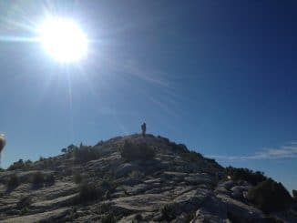Ein Berggipfel mit einem Mann auf der Spitze mit Sonne